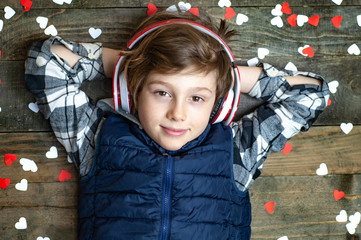 The boy listens to music with headphones lying on a wooden background. Around the white and red...