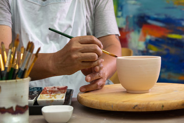 Hand on  working In his pottery studio. Ceramic workshop. Paint on clay cup in the pottery.