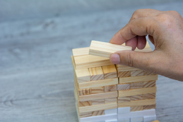 Man's hand holding a top of wooden blocks over wooden block ,business and management concept.