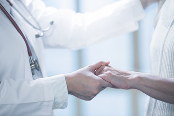 Medical doctor reassuring patient by holding patient’s hands in hospital setting