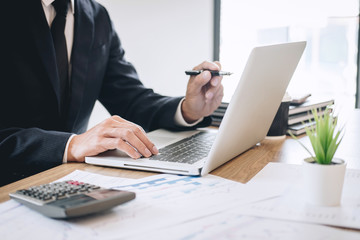 Fototapeta premium Businessman working new project on laptop computer with report document and analyze, calculating financial data on graph documents, doing finance making notes statistics