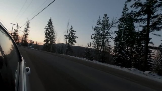 Driving silver car down windy road down mountain, with red sunset