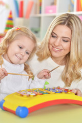 Fototapeta premium Close up portrait of mother with little daughter playing on musical instrument