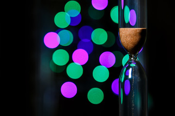 Hourglass in the center. Sand strews down on  christmas background, bokeh christmas lights. 
