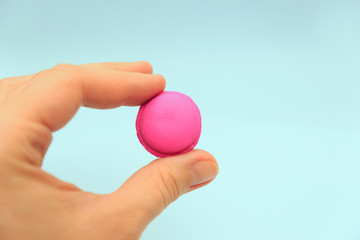 Female fingers hold a pink macaroon on a blue background. Rubber fake, bad imitation	
