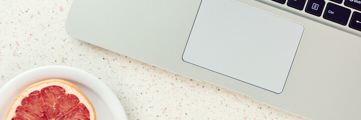 grapefruit on plate and laptop keybord on the table panorama