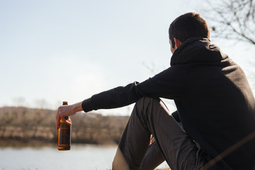 A young man drinks alcohol outdoors. Loneliness, problems in life.