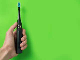 Electric sonic toothbrush in hand on green color background with copyspace