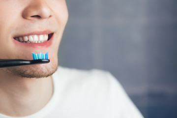 A young man with healthy white teeth uses an electric toothbrush
