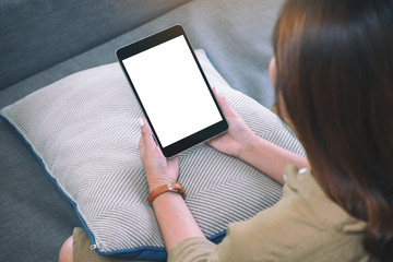 Mockup image of a woman holding black tablet pc with blank white desktop screen  while sitting in living room with feeling relaxed