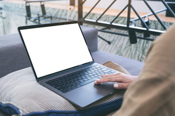 Mockup image of a woman using and touching on laptop touchpad with blank white screen while sitting in living room