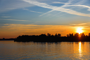 Bright and colorful sunset on the river. The sun hides behind the trees in the evening. Glare of the setting sun on the water.