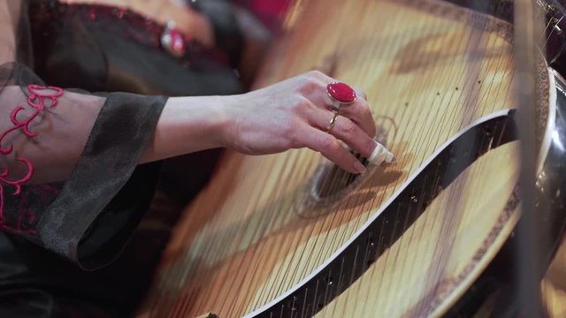 Close-up of a female musician's hand playing the strings of a bandura as she gently rocks back and forth.