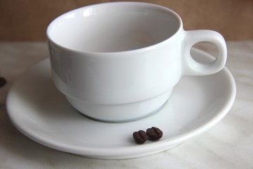 Cup and saucer, two coffee beans on a gray table top.