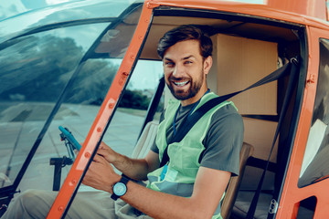 Cheerful good-looking man sitting on the front seat of the helicopter