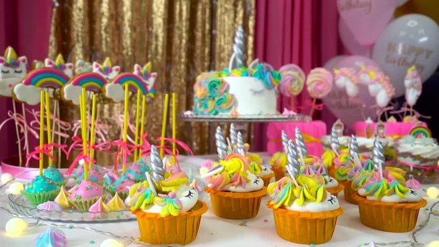Decorated children's birthday party with tasty cupcakes, colourful lollipops and unicorn cake