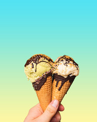 Ice cream in the cones held in the palm of your hand. Wafers and dessert with chocolate topping and colored sprinkles on a pastel background. Sweet and cold dessert with pistachio and vanilla flavor.