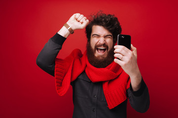 Winner guy, holding a smartphone and celebrating with rised hand over red background