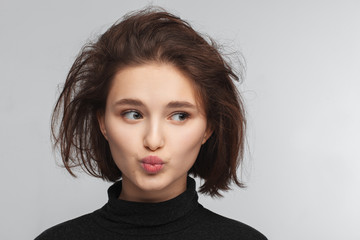 Portrait of a beautiful teen girl in a black sweater on a gray background. Combed up hair