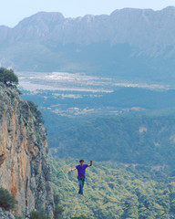 Obraz premium A man is walking along a stretched sling. Highline in the mountains. Man catches balance. Performance of a tightrope walker in nature. Highliner on the background of valley.
