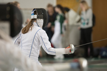 A girl with long hair having fencing duel on tournament. A girl holding a saber