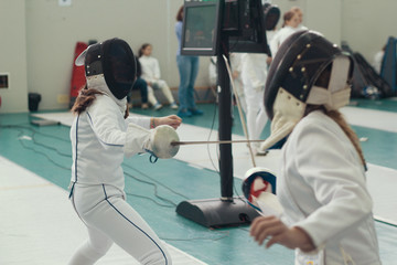 Two young girls fencers having fencing duel on tournament