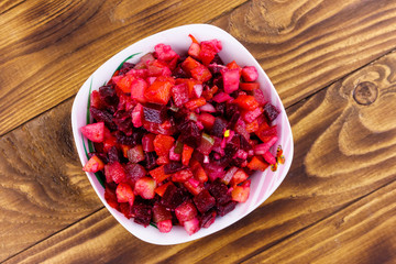 Traditional russian salad vinaigrette with beetroot, carrot, potato, onion and pickled cucumbers on wooden table. Top view