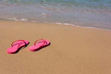 Fototapeta na wymiar pink flip-flops on yellow sand at the water's edge on the beach