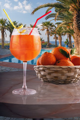a glass of cold drink and a basket of fruit on the table of the cafe against the background of the pool and the sea