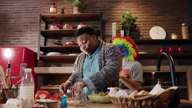 Funny shot with young african american man cook cut salad dance sing in the kitchen at home background man clown dancing smile happy food fresh healthy vegetables dinner portrait close up slow motion