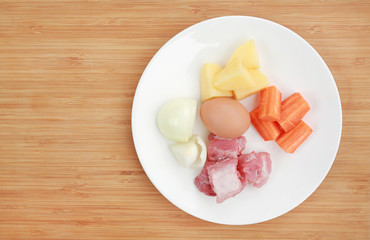 Carrot, egg, onion, pork bone and potato on white plate against wooden background Ingredients for boiling soup.