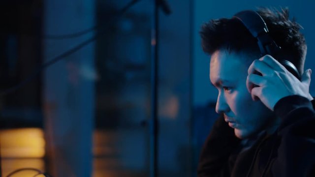 cybercrime, hacking and technology concept - asian male hacker putting headphones on for wiretapping or using computer for cyber attack and drinking coffee in dark room at night