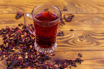 Glass cup of red hibiscus tea (carcade, roselle) on wooden table