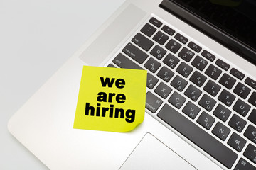 Sticky note on laptop with hiring text .