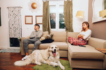 Young angry couple separated on sofa whit their dog