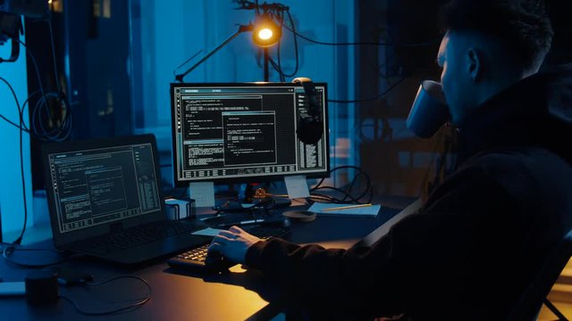 cybercrime, hacking and technology concept - asian male hacker writing code or using computer virus program for cyber attack and drinking coffee in dark room at night
