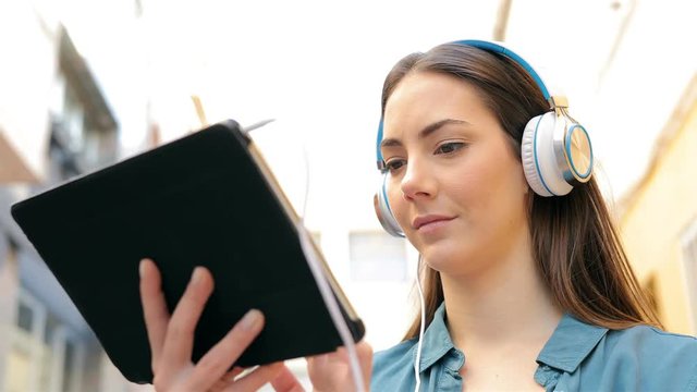 Serious woman using a tablet and headphones to browse online content in the street