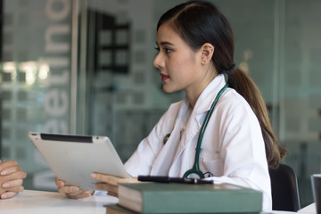 Female Asian doctor using a digital tablet & wearing a white coat.