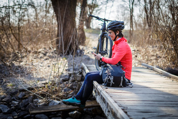 female cyclist listens to music while relaxing on the bridge in the forest