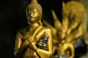 Close up view and low light of gold Buddha statue with coins on a hand in temple of Thailand. Monastery is place of religious importance and public for general people either Thai and foreign visitors.