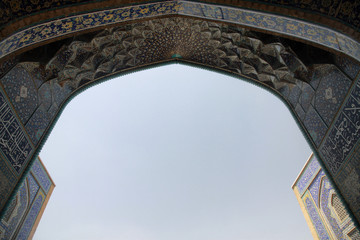 niebieska mozaika zdobiąca sklepienie łuku przy wyjsciu z zabytkowego meczetu w iranie i niebieskie niebo w tle - obrazy, fototapety, plakaty