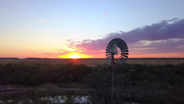 A windmill stays still on a calm day, bird flying out of shot, colorful sunset on the horizon.