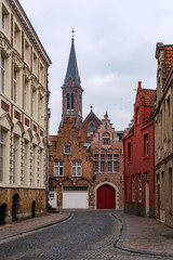 Naklejka na ściany i meble Old street of Bruges with traditional medieval houses of red brick with Heilig Hartkerk, former Jesuit church, tower in the background. Cityscape of Bruges streets.