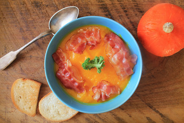 Creamy pumpkin soup served with crispy bacon on wooden background .