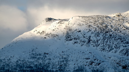 Peak Nabal in Stora Sj&ouml;fallets Nationalpark Lapland Sweden illuminated by sunrise sun spot during winter with snow, rocks, trees, clouds, view from Vakkotavare