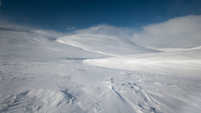 Sunny winter snowfields and rolling hills in Stora Sj&ouml;fallets Nationalpark Lapland Sweden along Kungsleden with deep blue sky and clouds