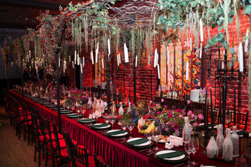 Table wedding decor in red and black tones. Pink, blue and red flowers bouquet and candles in bottles.