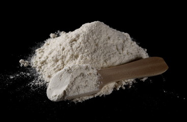 Wheat flour pile with wooden spoon isolated on black background, powder texture