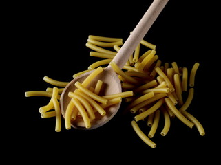 Macaroni, raw pasta with wooden spoon isolated on black background