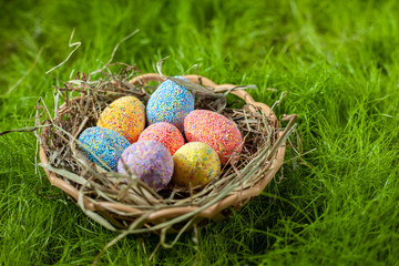 Colored decorative Easter eggs in a basket with hay on a green lawn